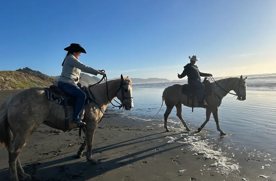 Two riders in western hats on the beach below the bluffs, in late afternoon light